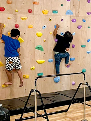 ボルダリングの壁をよじ登る小学生の児童