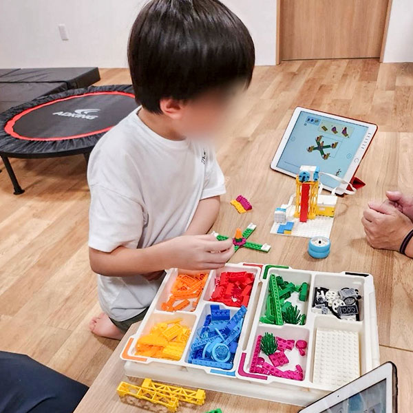 タブレットでレゴのプログラミングソフトの画面を見ながらレゴブロックを組み立てる小学生の男の子