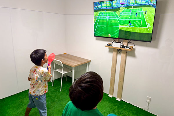 大画面モニターでSwitchのテニスゲームを楽しむ小学生の児童